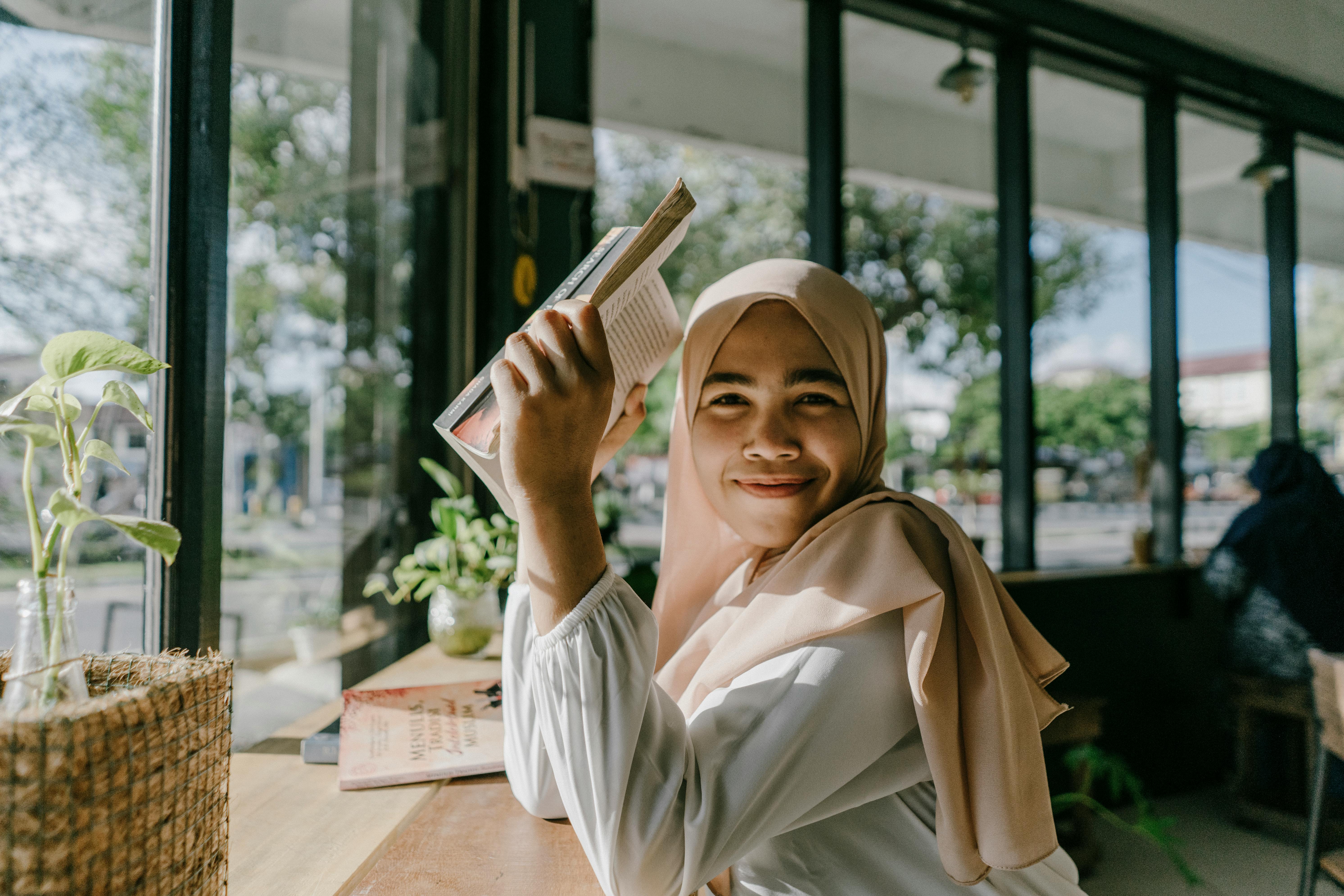 An adult learner reading a book by a window in a café.